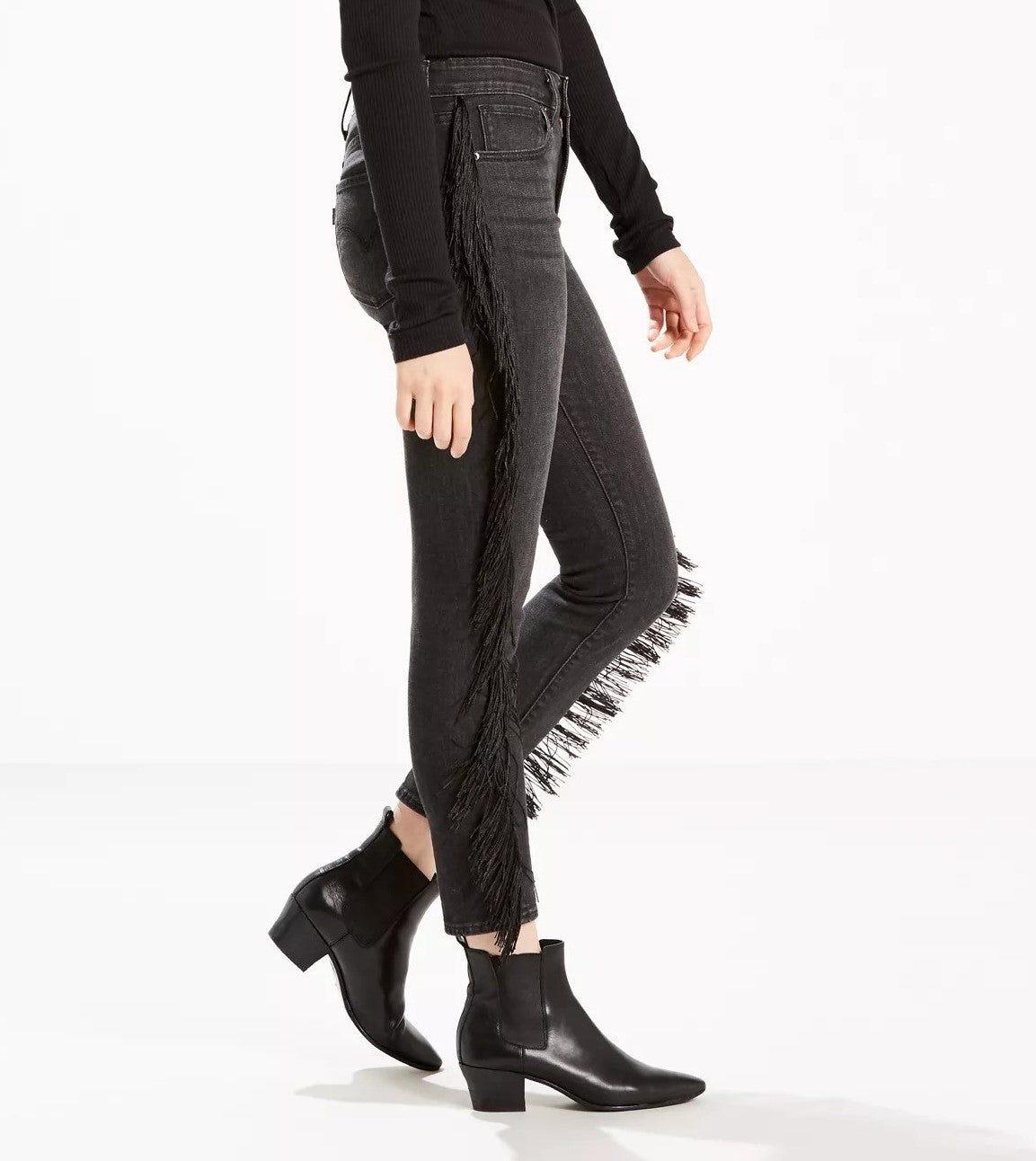 A person wearing black boots and trendy Levi's Limited 721 Fringe-Trim Skinny Ankle Jeans Black Size 24 with fringe trim on the side, showcasing a fashionable street style look.